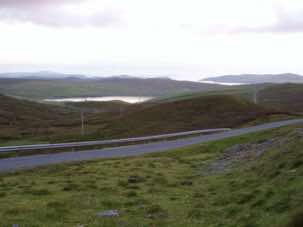The road just past Gonfirth Loch, with the road leading to Grobsness on the right, with Muckle Roe behind it. The first headland, with the little island, is Vementry Isle, and the long, low island behind it is Papa Stour. Next stop. Greenland!                                                      